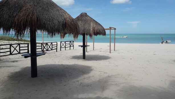 A beach with thatched umbrellas and a wooden fence. - Hotel San Julio (Celestún)