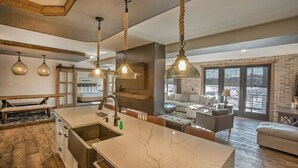 A modern kitchen with a marble countertop, hanging pendant lights, and a large window overlooking a cityscape.