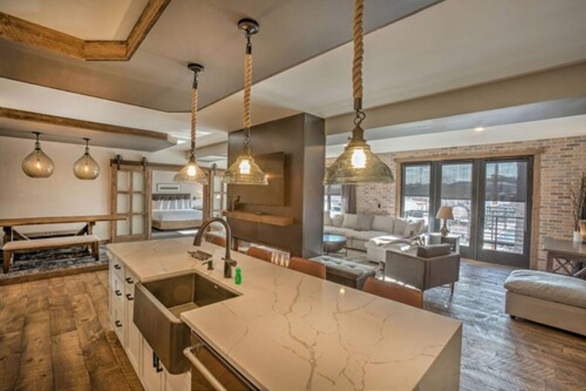 Uma cozinha moderna com bancada de mármore, luminárias pendentes e uma grande janela com vista para a cidade.