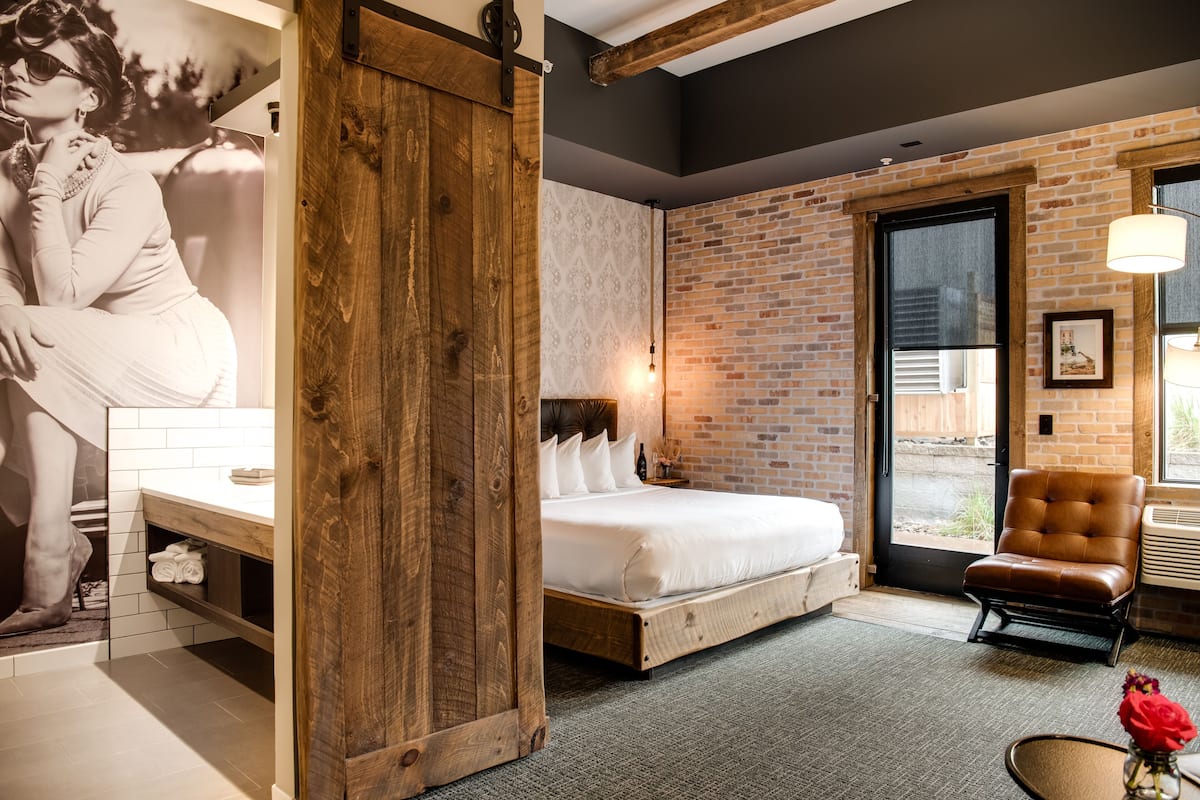 Quarto moderno com uma cama grande, guarda-roupa de madeira, parede de tijolo e vista através de uma porta de vidro.