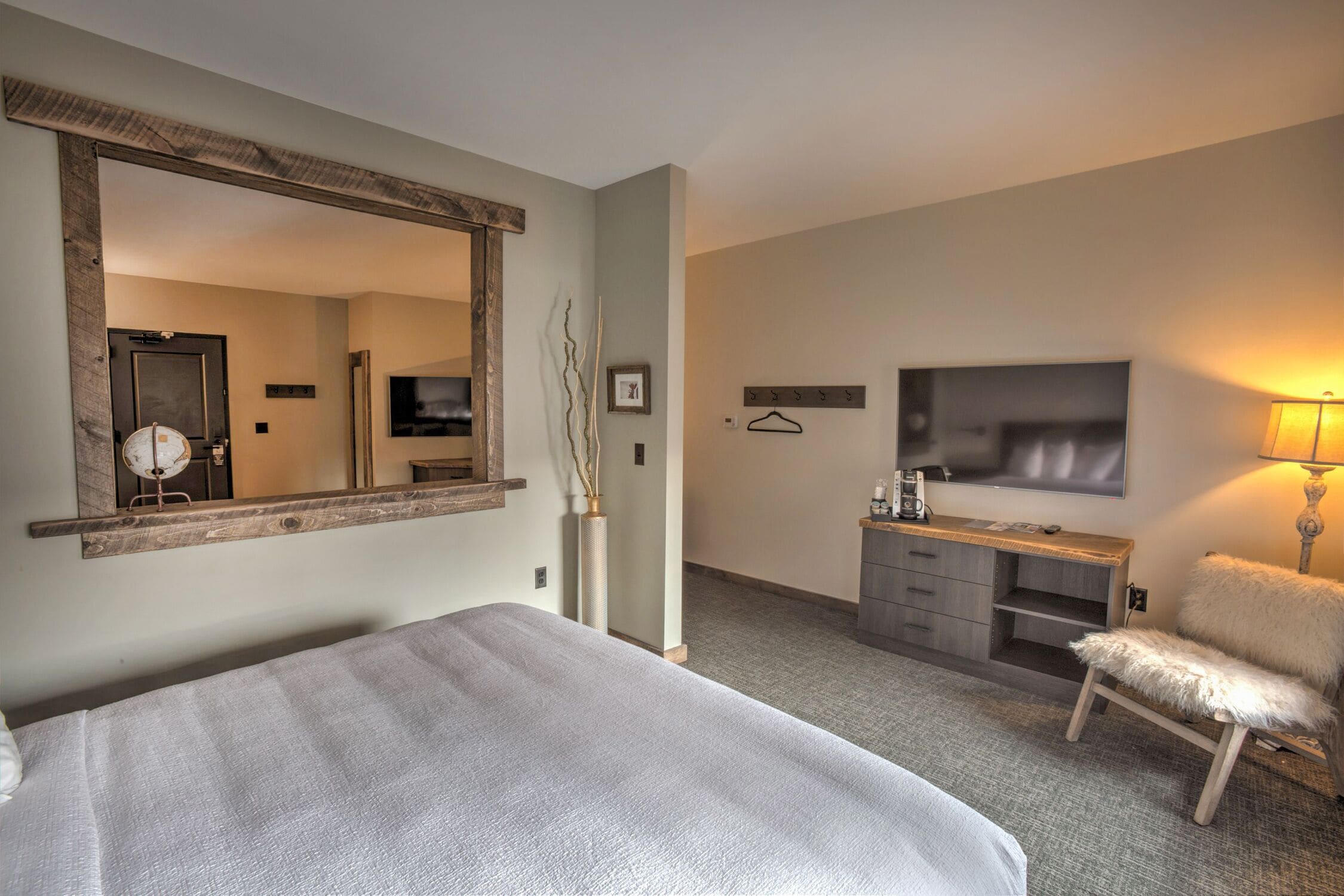 Ett hotellrum med en stor säng, en spegel, en byrå, en stol, en tv och en lampa.