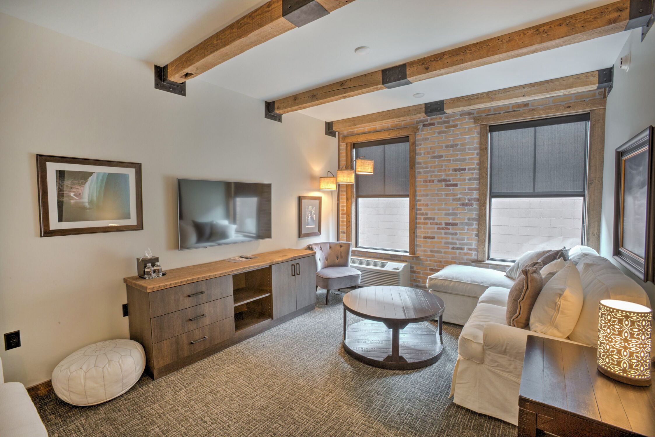 A modern living room with exposed wooden beams, a fireplace, a large window, and a cozy seating area.