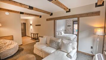 Habitación de hotel con un sofá blanco, un sillón redondo de mimbre, una cama y vigas de madera a la vista en el techo.