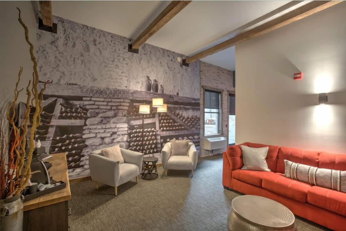Sala de estar com painel de parede de pedra, dois poltronas brancas, um sofá vermelho e uma mesa de centro redonda.