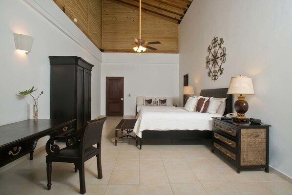 A bedroom with a bed, bedside tables, a desk, a chair, a ceiling fan, and a decorative wall piece.