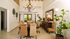 A dining area with a wooden ceiling, a chandelier, wicker furniture, and a large mirror.