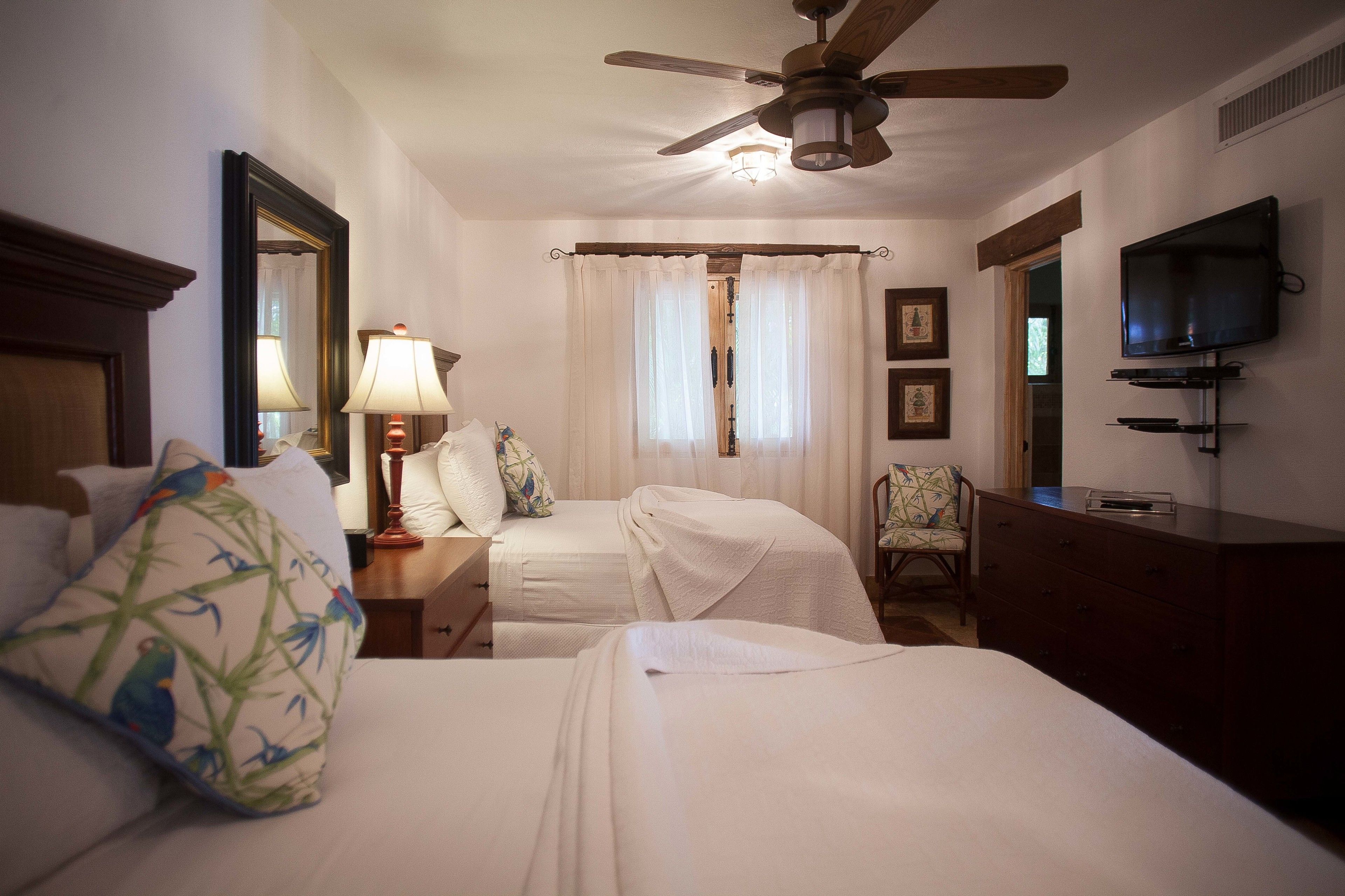 A hotel room with two beds, a ceiling fan, a TV, and a chair.