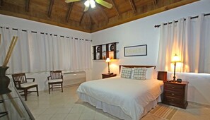 A hotel room with a large bed, two bedside tables with lamps, a wooden headboard, a wall clock, a framed picture, and a window with curtains.