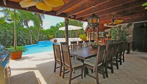 An outdoor dining area with a pool, wooden chairs, and a table.