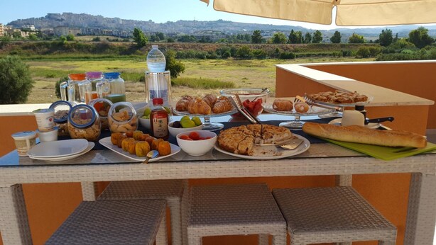 A buffet table with various food items and condiments, set against a scenic outdoor backdrop. - Locanda degli Scrittori (Agrigento)
