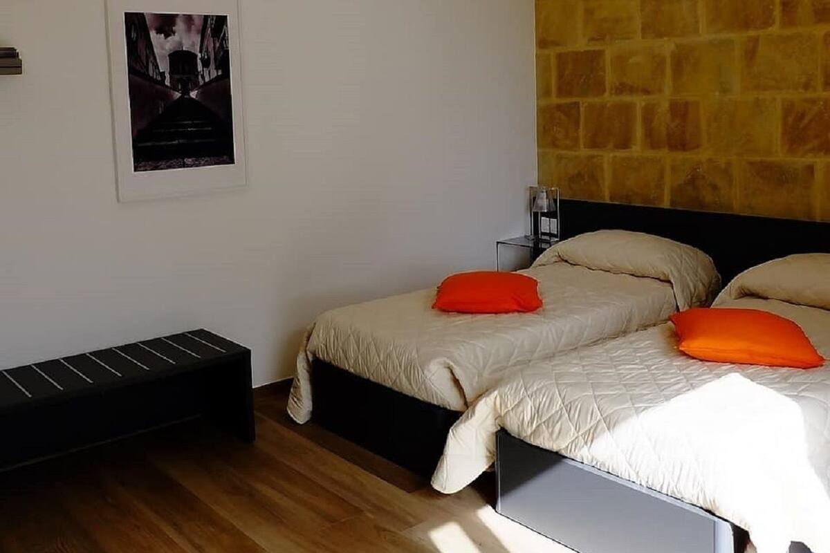 A modern bedroom with two beds, a stone accent wall, a framed picture, and a bench.