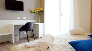 A hotel room with a bed, a desk, a chair, a TV, and a window with a view. - Locanda degli Scrittori (Agrigento)