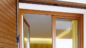 A bedroom with a bed, a sliding glass door leading to a balcony, and a stone wall. - Locanda degli Scrittori (Agrigento)
