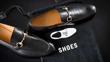 A pair of black leather shoes with gold chains on a black fabric with the word "SHOES" and a shoe icon.
