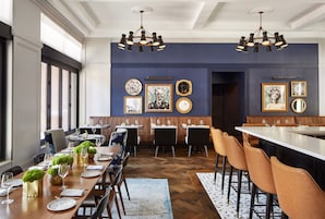 A dining area with a long wooden table, multiple chairs, and a high ceiling with chandeliers.
