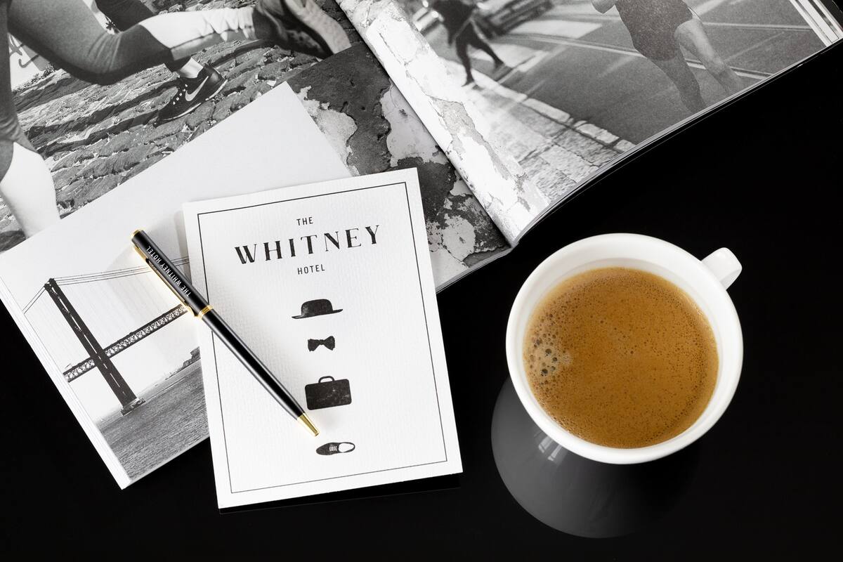 En sort-hvid brochure for The Whitney Hotel, en pen og en kop kaffe på et bord.