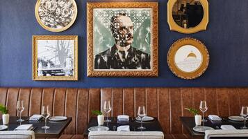 Interior de un restaurante con pared azul, obras de arte enmarcadas y disposición de cabinas.