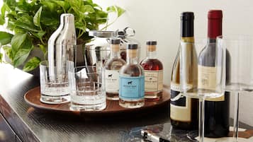 A tray with various bottles and glasses, likely for serving drinks, placed on a wooden table with a potted plant in the background.