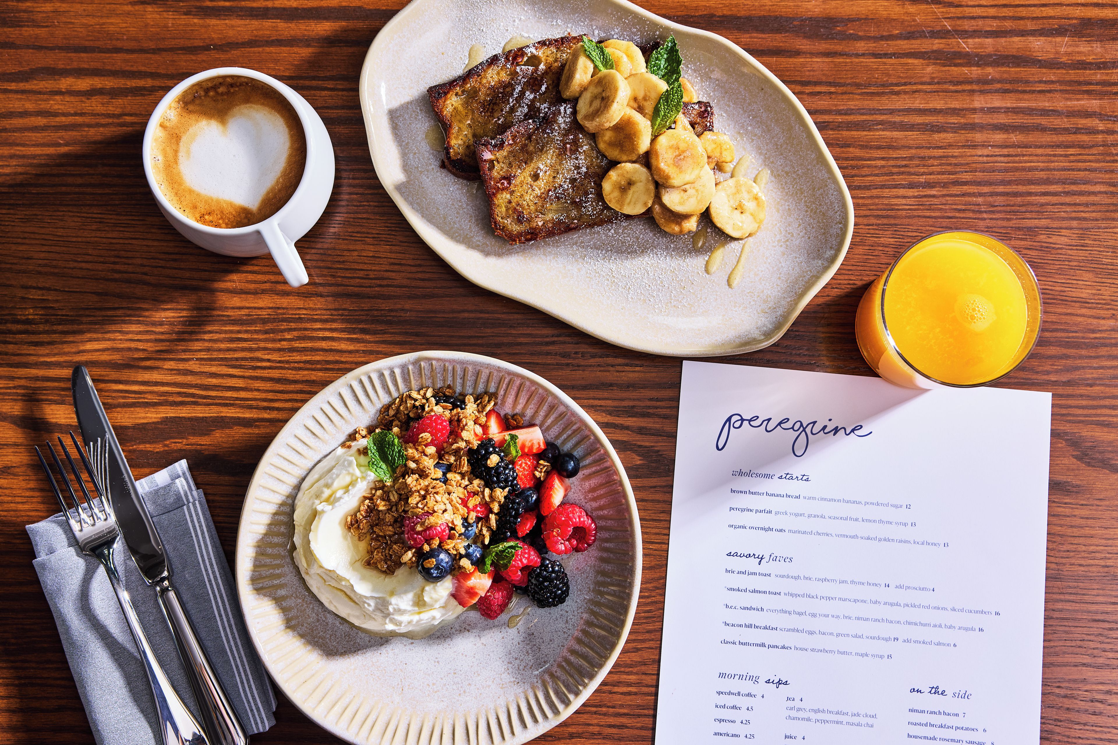 Una escena de desayuno con un menú, un plato de tortitas con fruta, una taza de café y un vaso de zumo de naranja.