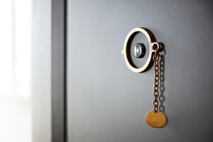 Een sleutelhanger met een metalen ring en een rond aanhangertje waarop 'W.H' gegraveerd staat, hangend aan een grijze deur.
