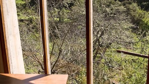 Une table et un banc en bois se trouvent dans une pièce dotée de grandes fenêtres donnant sur une zone boisée.