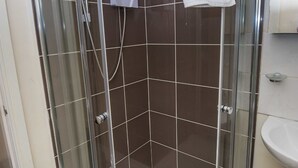 Eine Duschkabine mit einer weißen Handtuch an der Tür, einer Handbrause und einem Seifenspender an der Wand.