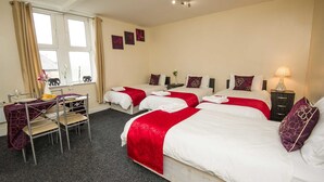 Ein Hotelzimmer mit drei Betten, einem Essbereich mit Tisch und Stühlen sowie einem Fenster mit Vorhängen.