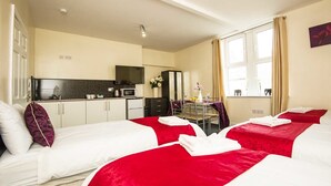 Ein Hotelzimmer mit zwei Betten, einer Küchenzeile, einem Essbereich und einem großen Fenster.