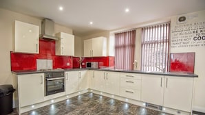 A modern kitchen with white cabinets, a red backsplash, and a stainless steel range hood. - Snooze Apartments Flat 52 (Bradford)