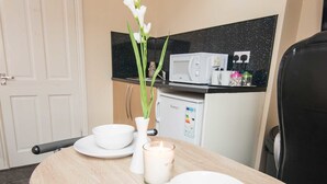 A dining table with white plates and a candle, a white vase with flowers, and a microwave in the background. - Snooze Apartments Flat 52 (Bradford)
