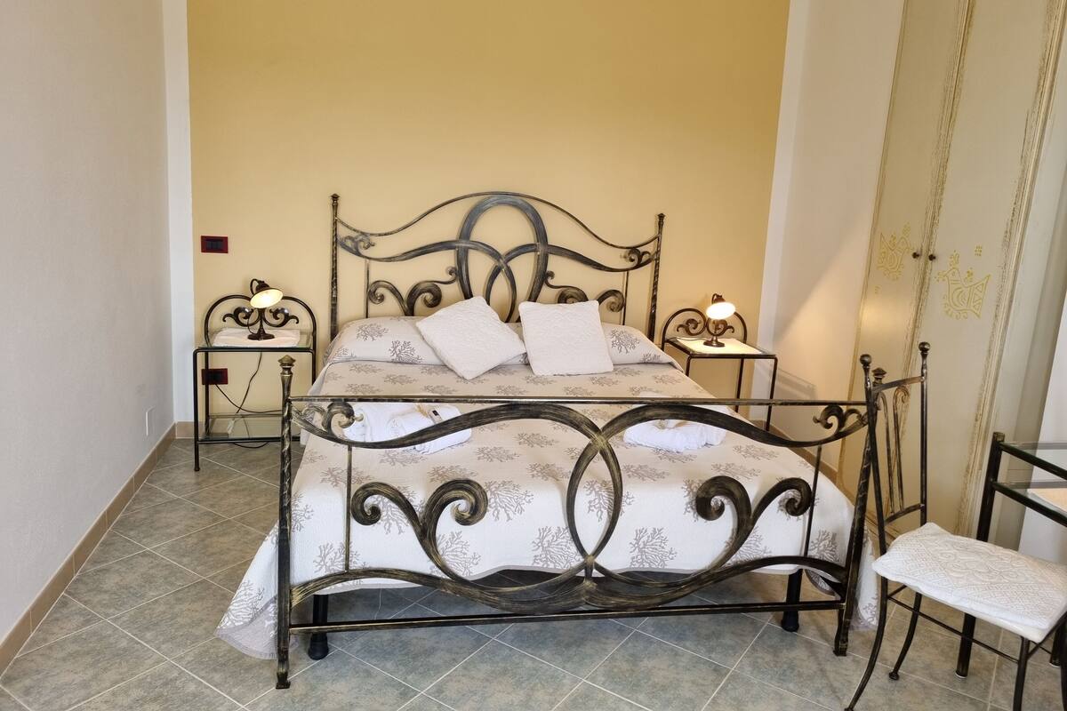 Una cama con estructura metálica, dos mesitas de noche con lámparas, una silla y un armario con paneles decorativos.