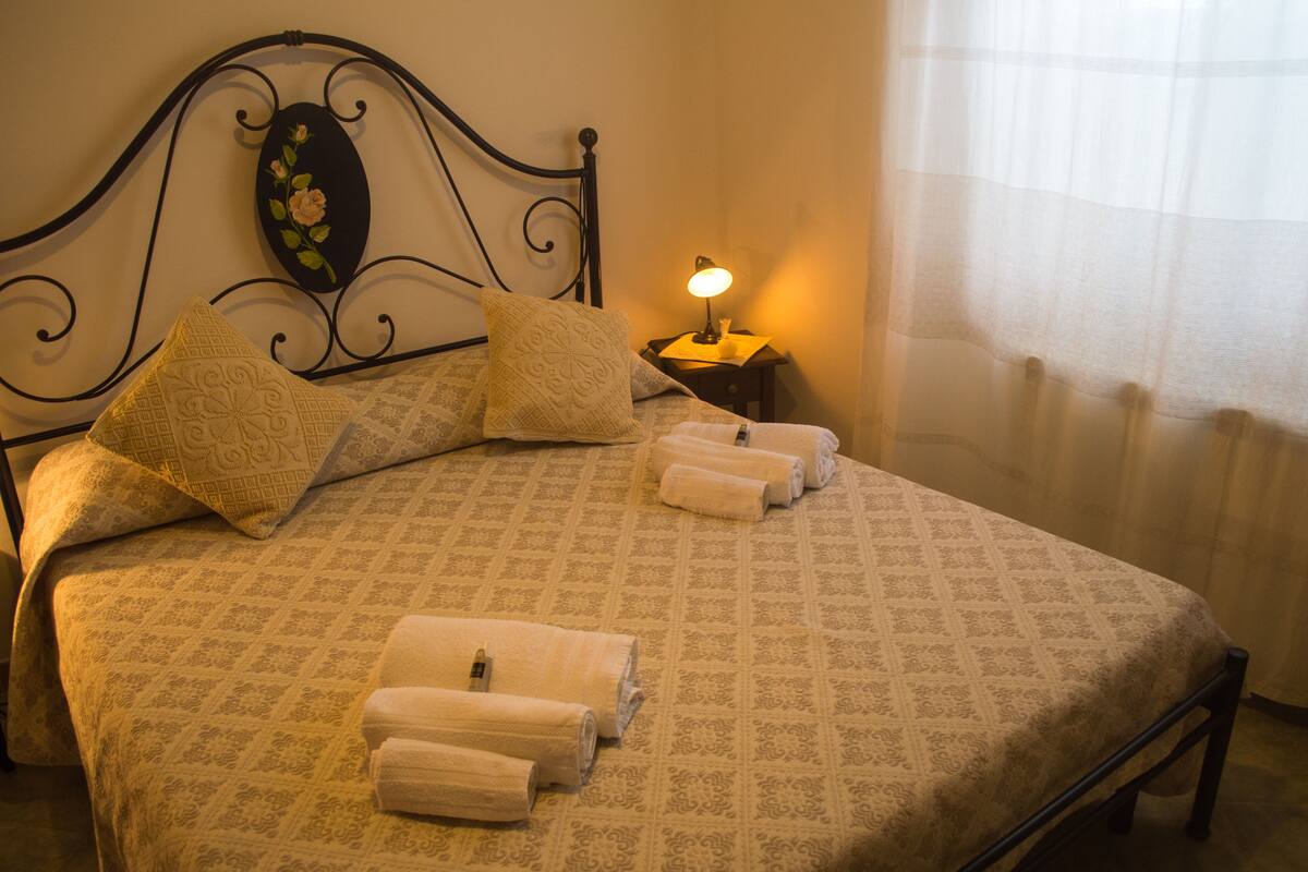 Una cama bien hecha con un edredón estampado, dos almohadas y toallas enrolladas.