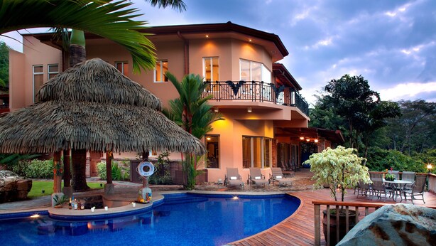 A resort with a swimming pool, a thatched-roof structure, and a dining area with outdoor seating. - Casa Oasis (Jacó)