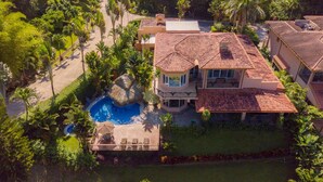 A large house with a swimming pool, surrounded by lush greenery and palm trees. - Casa Oasis (Jacó)