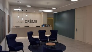 Un espace d’accueil moderne avec un comptoir de réception portant l’inscription « URBAN CRÈME », agrémenté de luminaires ronds au plafond, de chaises bleu foncé et d’un sol carrelé.