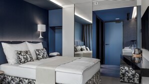 Une chambre d’hôtel moderne avec un grand lit, une table de chevet, un miroir et une salle de bain visible à travers une porte ouverte.