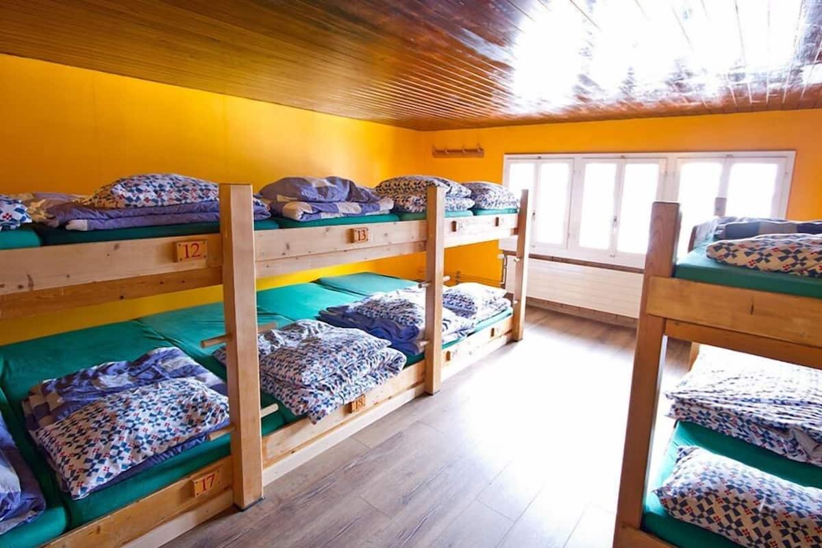 Um dormitório com beliches, piso de madeira e uma janela com persianas brancas.