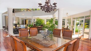 A spacious dining area with a glass-top table surrounded by wicker chairs, a chandelier, and a view of the outdoors. - Villas Los Pinos by Casa de Campo Resort & Villas (La Romana)