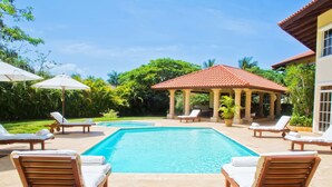 A swimming pool with lounge chairs and umbrellas, surrounded by lush greenery and a gazebo. - Villas Los Pinos by Casa de Campo Resort & Villas (La Romana)