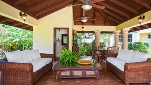 A covered outdoor seating area with wicker furniture, a glass-top coffee table, and a ceiling fan. - Villas Los Pinos by Casa de Campo Resort & Villas (La Romana)