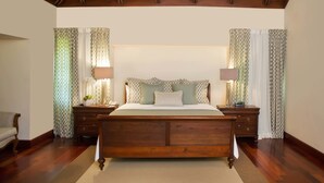 A bedroom with a wooden bed, patterned curtains, and a nightstand with a lamp. - Villas Los Pinos by Casa de Campo Resort & Villas (La Romana)