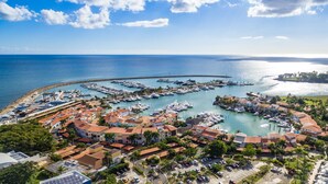 Vista aérea de un puerto deportivo costero con numerosas embarcaciones amarradas, rodeado de edificios residenciales con tejados de tejas rojas y un cielo azul despejado.