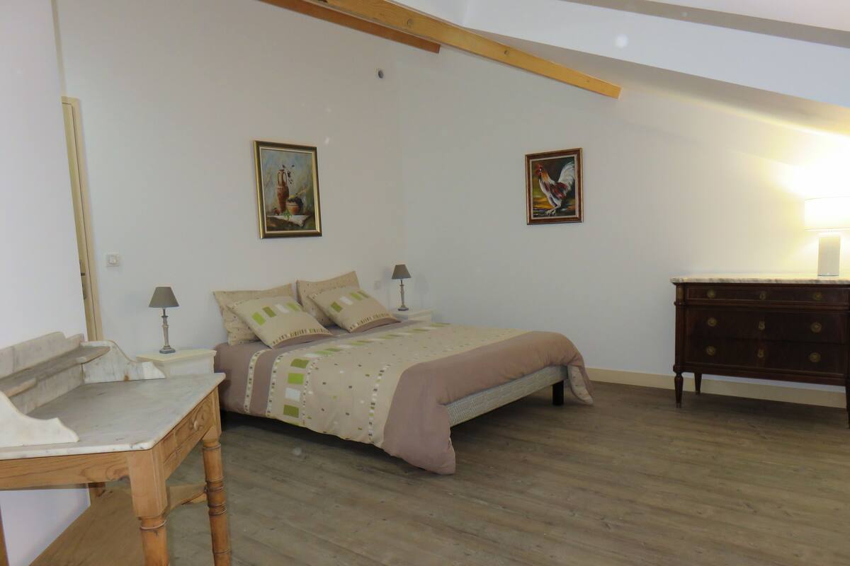 A bedroom with a bed, bedside tables, a dresser, and two wall-mounted paintings.