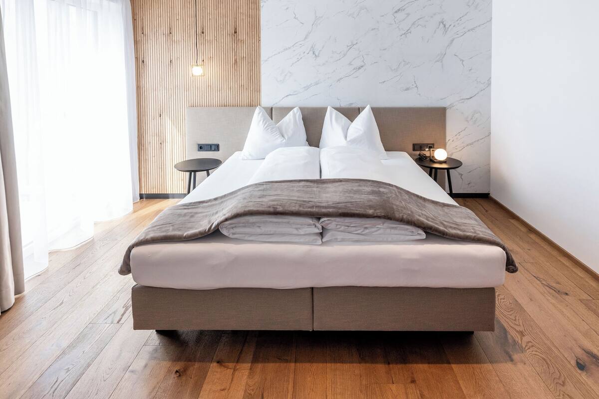 Ein modernes Hotelzimmer mit einem großen Bett, Holzboden, Marmorwand und einem kleinen Nachttisch mit Lampe.