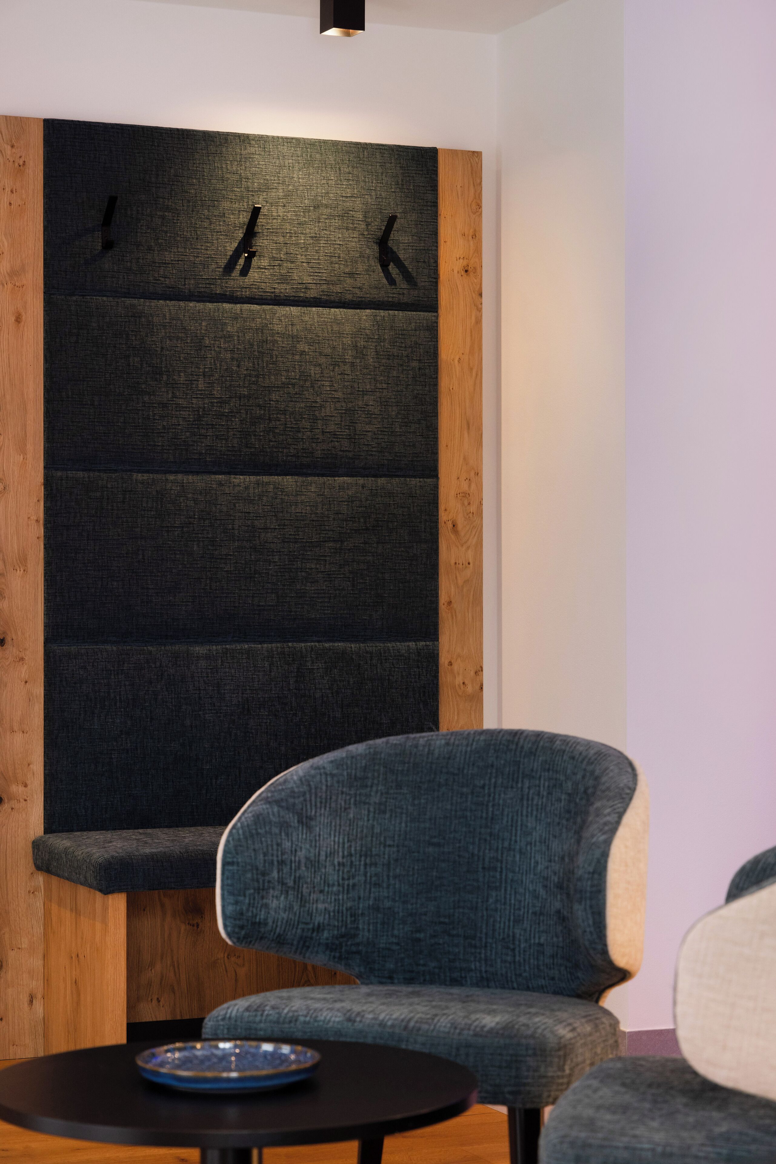 A modern room with a dark textured wall, a wooden accent panel, and a blue upholstered chair.