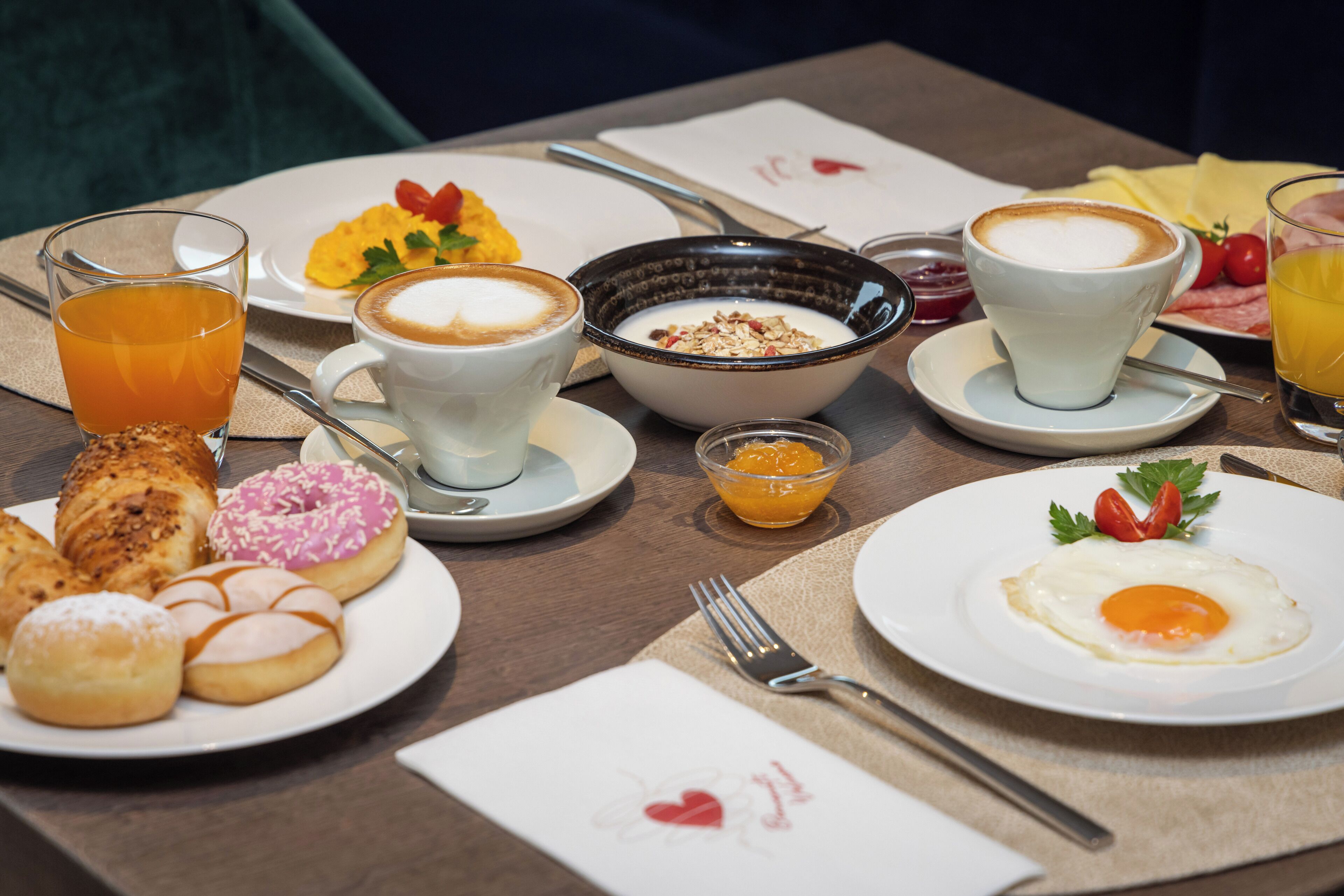A breakfast table with various food items, including pastries, a bowl of cereal, a cup of coffee, and a glass of orange juice.