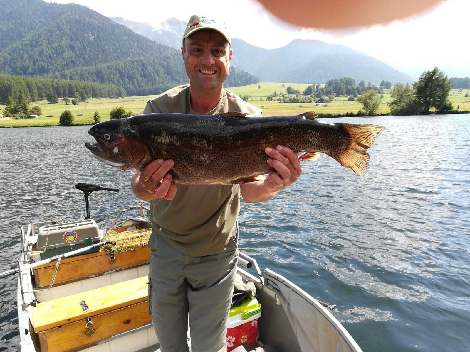 Eine Person hält einen Fisch in einem Boot vor einer bergigen Landschaft.