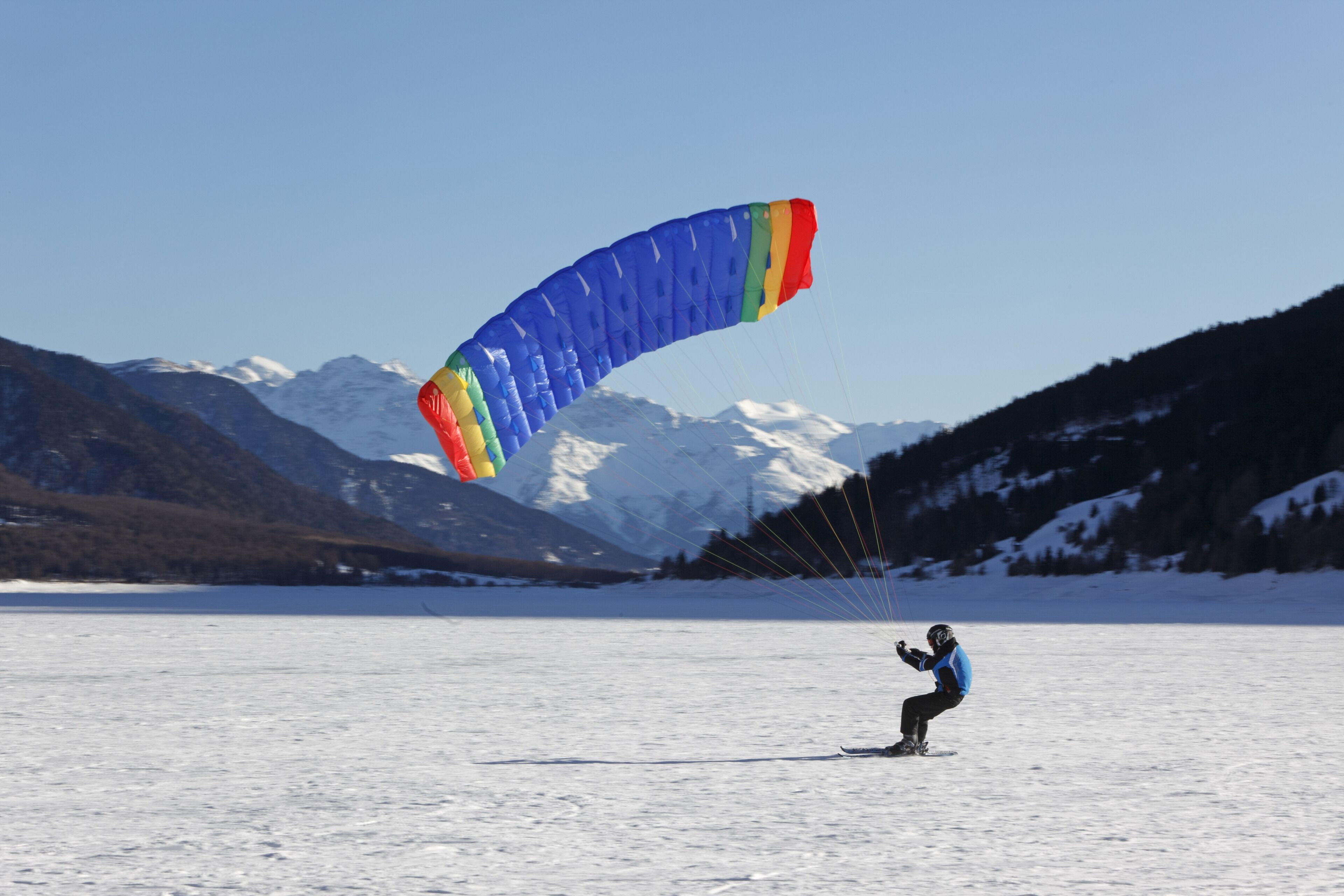 A person kiteboarding on a snowy lake with mountains in the background.