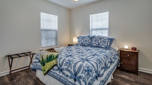 A bedroom with a bed, two bedside tables, a nightstand, a ceiling fan, and two windows with blinds.