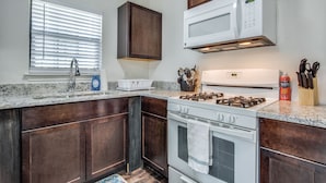A kitchen with dark wood cabinets, a white stove, a microwave, and a window with blinds.